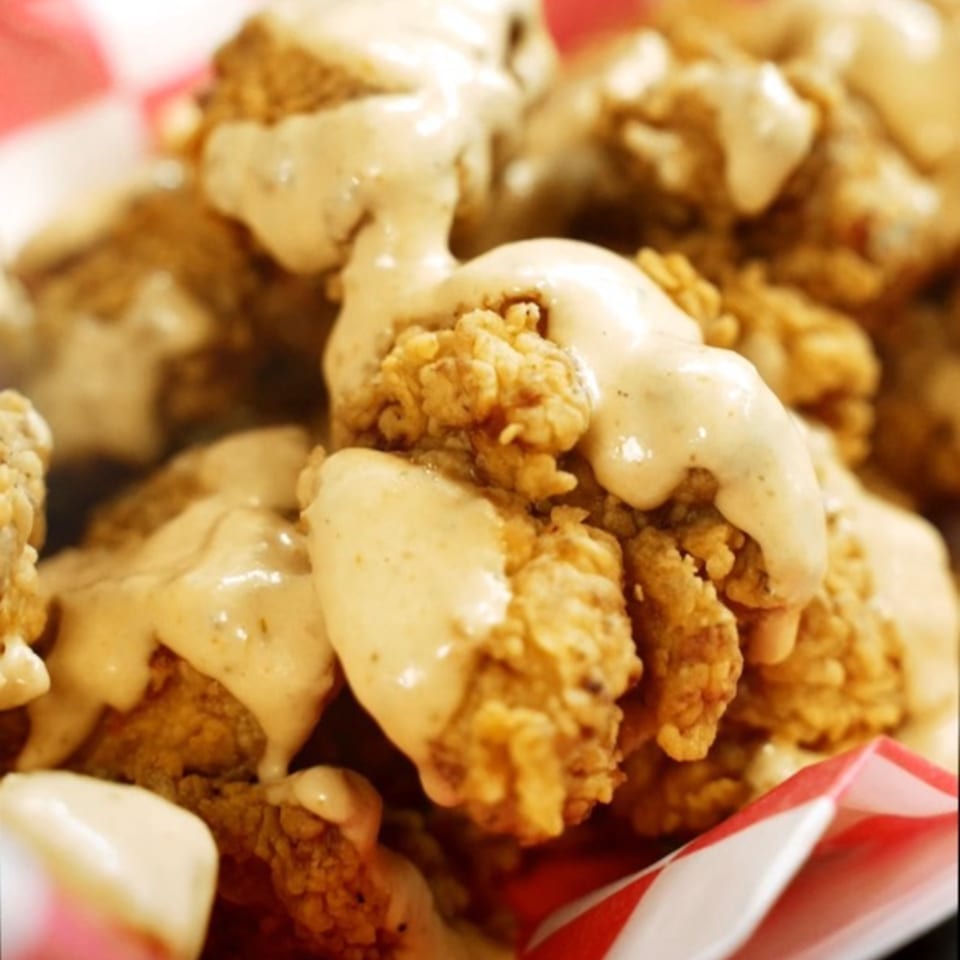 Crispy fried chicken pieces from The Halal Hen, generously drizzled with a creamy sauce.