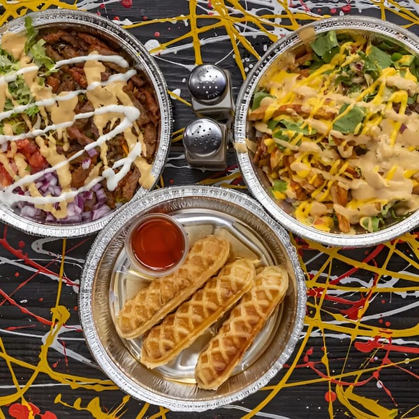 Two foil containers of Halal Hen bowls with sauces, and a side of waffle fries with ketchup.