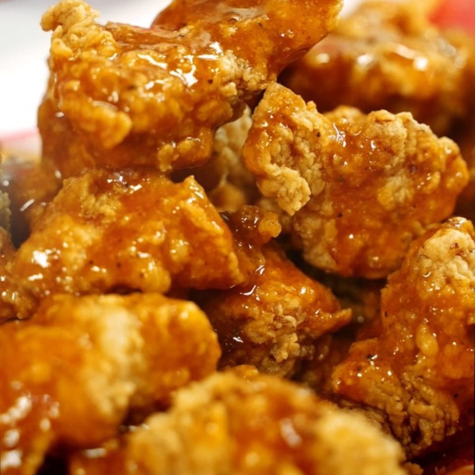 Close-up of crispy, golden-brown Halal Hen chicken bites generously coated in a glistening orange sauce.