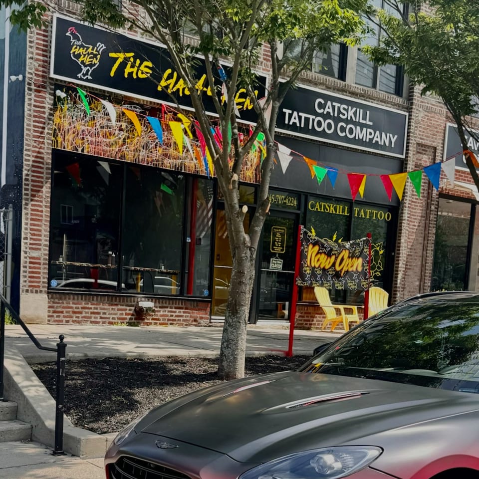 The Halal Hen restaurant exterior with a black sign, colorful bunting, and a parked car.