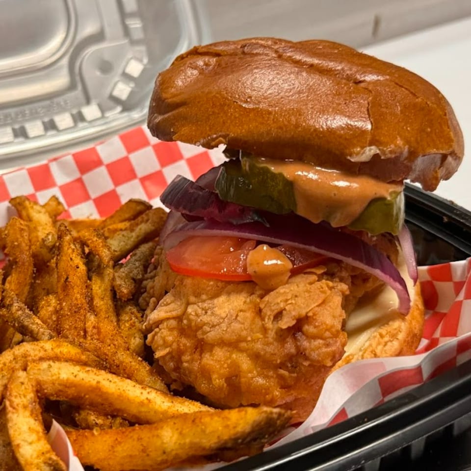 Halal Hen fried chicken sandwich with pickles, onions, tomatoes, and fries in a takeout container.